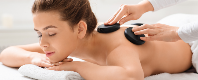 woman lying on massage table with stones on her back for a hand and stone massage